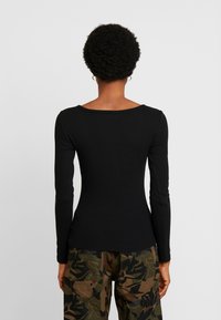 Langarmige zwarte top met een ronde halslijn, gemaakt van ribbelstof. Draag het met camouflage-gepatenteerde broeken, wat een aansluitende silhouette laat zien.