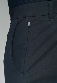 Mørknavy bukser med et glat, tekstureret stof; har en lynlås lomme på siden til sikker opbevaring. Tætsiddende design med et moderne snit.