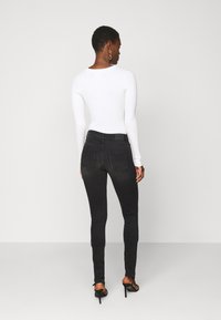 Jeans skinny pretos com um acabamento desbotado, apresentando dois bolsos traseiros e uma cintura alta, combinados com uma blusa justa de mangas longas branca.