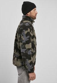 Fleece jacket with a camouflage pattern in shades of green and gray. Features a high collar, zip closure, and textured fabric.