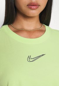 Grön bomull t-shirt med en svart Nike-logotyp på bröstet. Rundhalsdesign, kort ärm och jämn textur. Guldpärlhalsband synligt.
