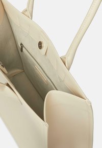 Beżowa torebka z gładkiej skóry, z miękkim wnętrzem z tkaniny, zamykaną na zamek kieszonką oraz z zatrzaskiem.