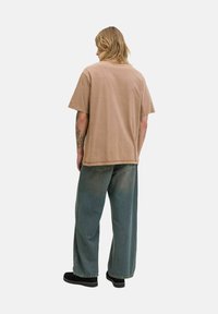 Brun kortærmet T-shirt, afslappet pasform, båret med løse blå denimjeans. Materialet virker blødt med en let falmet tekstur.