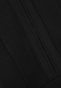 Schwarzes, mit Reißverschluss versehenes Kleidungsstück mit glatter Textur und kontrastierenden Abschnitten. Der Reißverschluss verläuft senkrecht entlang der Mitte.