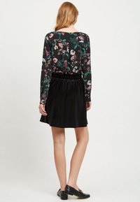 Jupe en velours noir avec une taille froncée, associée à un haut à manches longues à motif floral avec des tons sombres et des couleurs vives.