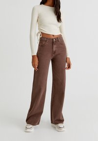 Browni levelejeansit valmistatud denimist, millel on tekstureeritud viimistlus, kombinatsioon kerge koorevärvi pikkade varrukatega topiga, millel on külgedel nöörid.