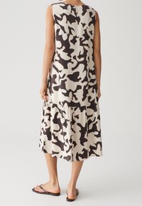 Robe midi sans manches à motif abstrait noir et blanc, jupe à volants, portée avec des sandales plates noires, vue de dos.