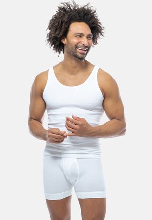 Canotta di cotone bianco e slip boxer, texture a costine, vestibilità aderente, senza motivi, indossata da un uomo con capelli ricci, sfondo neutro.