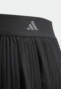 Falda negra plisada con una cintura ancha y lisa que presenta el logo reflectante de Adidas. Hecha de tejido ligero y texturizado.
