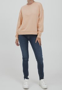 Felpa pescozzo con spalle cadute, abbinata a jeans skinny scuri e sneakers bianche. Tessuto morbido, vestibilità rilassata.