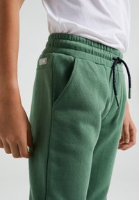 Gröna bomullssweatpants med elastisk midja, sidofickor och justerbar dragsko. Mjuk textur med en etikett på baksidan.