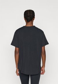 Juoda trumpomis rankovėmis marškinėliai su laisvu siluetu ir apvalia iškirpte, pasižymintys nuleistais pečiais ir subtiliais si�ūlės detalėmis gale.