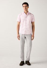 Chemise rose à manches courtes avec motif floral blanc, col boutonné, associée à un pantalon en lin gris clair et des chaussures marron.