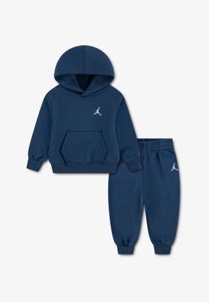 Tamsiai mėlynas džemperio su gobtuvu ir laisvalaikio kelnių komplektas, pagamintas iš medvilnės mišinio. Džemperis turi priekinę kišenę ir logotipą; laisvalaikio kelnės turi elastingą juosmenį ir rankogalius.