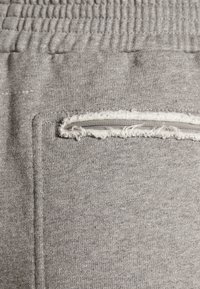 Grå mjukisbyxor med ett ribbat midjeband, en slitna dragkedjeficka och ett mjukt, texturerat tyg med ett lätt melerat mönster.