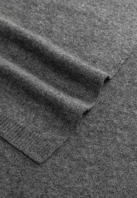Soft, folded dark gray wool sweater fabric showing knit texture and ribbed cuff detail.