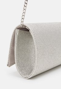 Borsa cilindrica argentata glitterata con pattina e sottile tracolla argentata su uno sfondo bianco.
