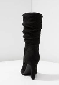 Botte haute en daim noir avec un design décontracté, bout pointu et talon fin. La texture est lisse, mettant en valeur son apparence élégante.