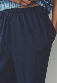 Pantaloni căptușiți de culoare bleumarin, confecționați dintr-un material moale, cu un brâu elastic și buzunare laterale, având o textură subtilă și o croială lejeră.