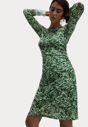 Zelené květinové šaty s dlouhými rukávy a těsným střihem. Mají strukturovaný vzor bílých a tmavě zelených květů.
