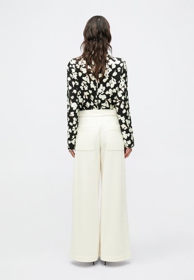 Melnbalta blūze ar ziedu rakstu un garām piedurknēm, kombinēta ar plašām krēmkrāsas biksēm ar aizmugurējām kabatām un gludu, teksturētu apdari.
