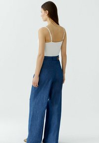 Weißes, figurbetontes Tanktop mit dünnen Trägern, kombiniert mit weitem blauen Denim-Hosen mit hoher Taille und dekorativer Schnalle.