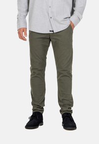 Pantalones de corte slim en color verde oliva, hechos de una mezcla de algodón. Combinados con una camisa de botones gris y zapatos negros de cordones. Textura suave, sin estampados.