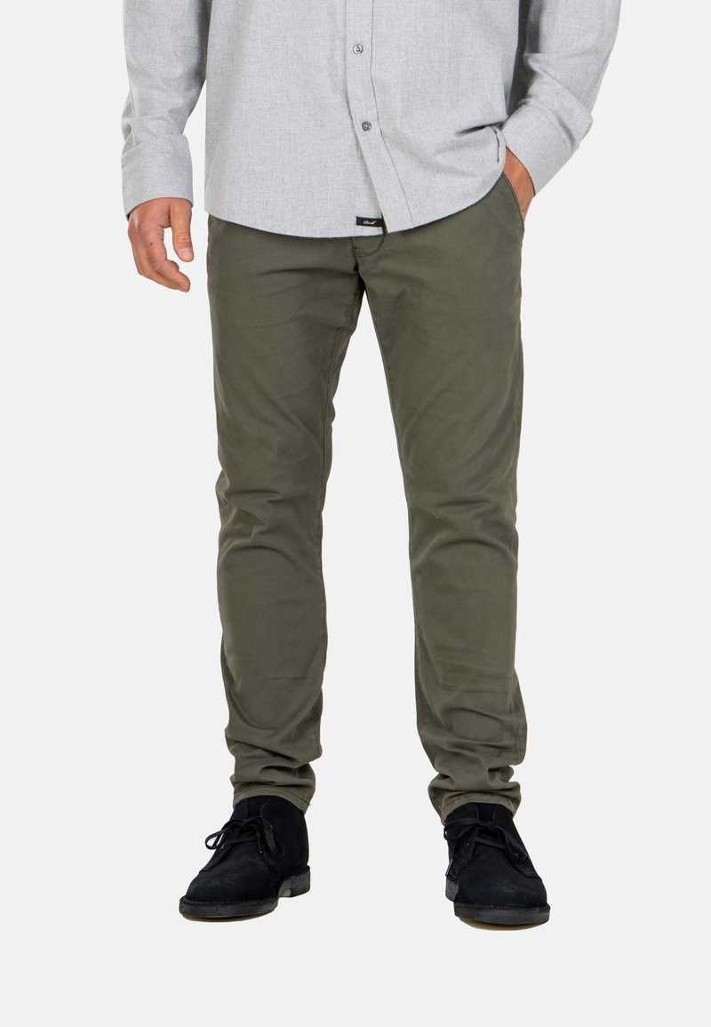 Pantalones de corte slim en color verde oliva, hechos de una mezcla de algodón. Combinados con una camisa de botones gris y zapatos negros de cordones. Textura suave, sin estampados.
