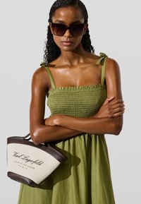 Roheline smock-kleid, millel on õhukesed rihmad, koos kreemi- ja pruunist käekotist, millel on logo. Sleek, sile tekstuur ja kaasaegne disain.