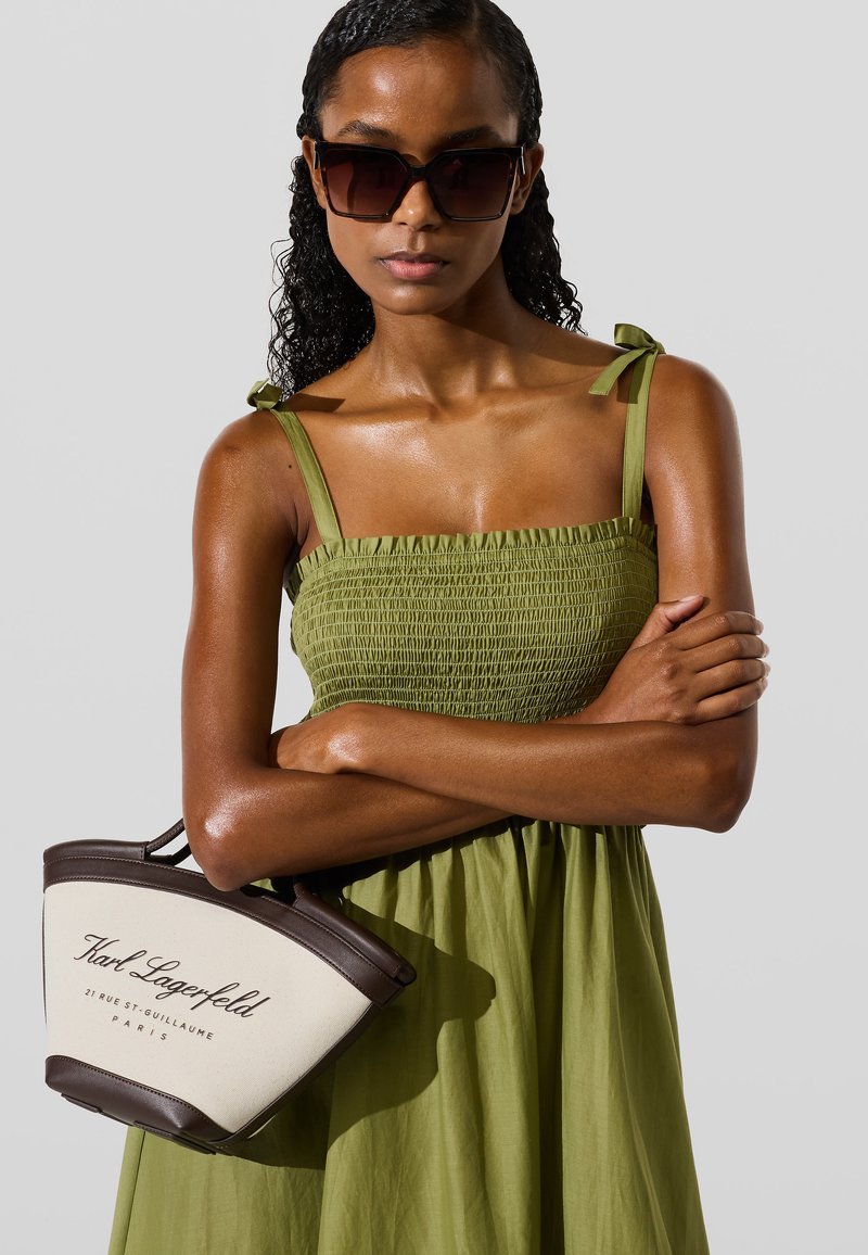 Roheline smock-kleid, millel on õhukesed rihmad, koos kreemi- ja pruunist käekotist, millel on logo. Sleek, sile tekstuur ja kaasaegne disain.