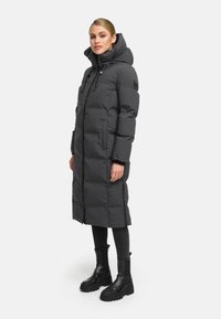 Long black puffer coat with a high collar, zip closure, and drawstring hood. It features two side pockets and a quilted pattern.