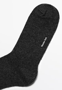 Black wool sock featuring a smooth texture and a knitted pattern. Prominent white label reads "Massimo Dutti." Rounded toe design.