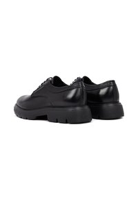 Zwarte leren schoenen met een ronde neus, een gladde textuur en een dikke rubberen zool. De achterkant heeft een iets verhoogde hak voor extra ondersteuning.
