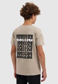 Beige katoenen t-shirt met een grote zwart-wit tekstgrafiek op de rug. Korte mouwen en een ronde halslijn, met een relaxte pasvorm.
