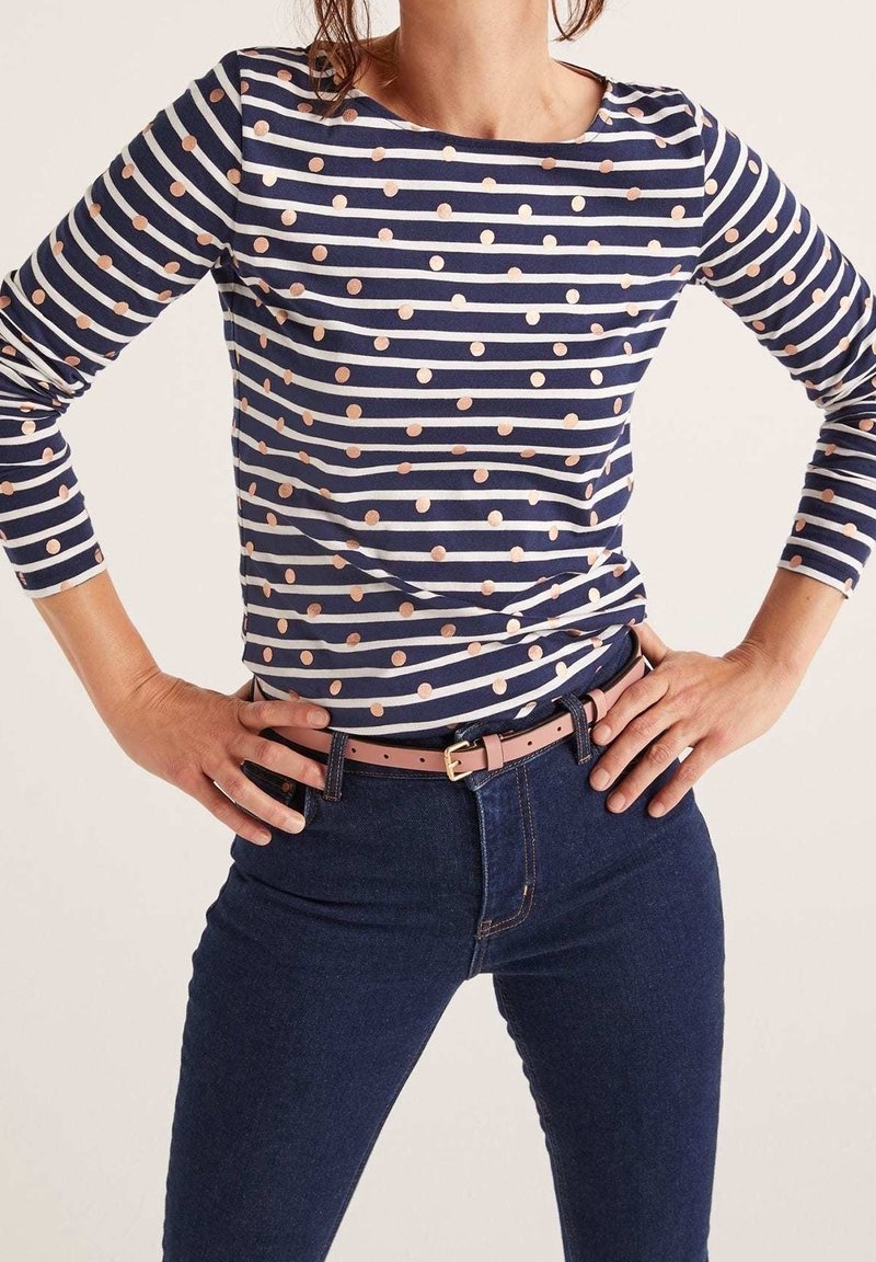 Marinblå och vit randig långärmad tröja med metalliska prickar; kombinerad med mörkblå jeans och ett ljust rosa bälte som framhäver midjan.