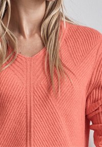 Korale sweter z dzianiny z dekoltem w serek, z pionowym prążkowaniem i teksturowanym wzorem. Miękka tkanina o luźnym kroju i strukturalnych detalach.