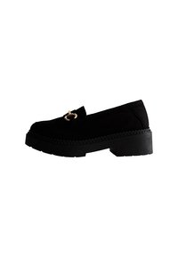 Mocasines de ante negro con un tacón grueso, que presentan un acento de metal de tono dorado y una suela texturizada. Diseño minimalista con un acabado suave.