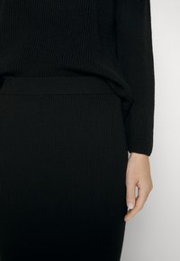 Svart ribbad tröja och kjolset med en strukturerad stickad mönster, figurnära passform och en slät midjeband.