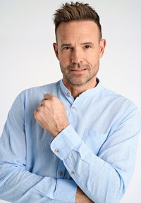 Jasnoniebieska koszula z kołnierzykiem mandaryńskim, wykonana z teksturowanej tkaniny. Posiada kieszeń na piersi i metalowe detale przy guzikach.