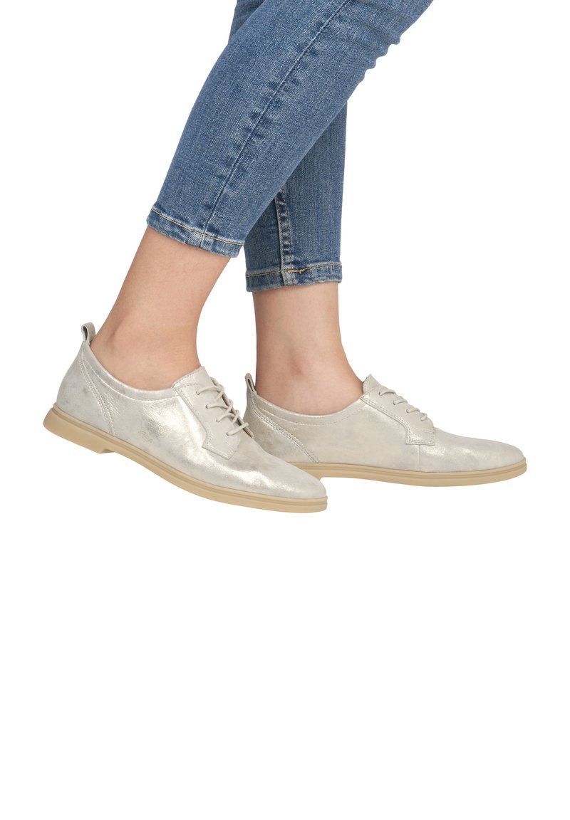 Chaussures en cuir métallique argenté avec une texture lisse, bout rond et semelle beige clair. Des lacets et un onglet au talon sont également présents.