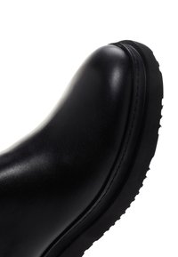 Bottine en cuir noir avec un bout arrondi, texture lisse, semelle en caoutchouc contrastante et détails de couture minimaux.