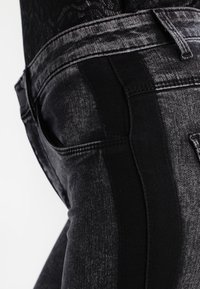 Pantalones vaqueros de mezclilla negra con un efecto de lavado en degradado desde tonos oscuros a más claros, con costuras detalladas a lo largo de las costuras y los bolsillos.