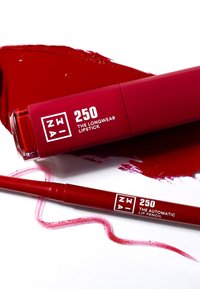 Röd läppstift och läppenna på vit bakgrund, med djärv förpackning och vit text. Slät textur med glansiga och matta ytor.