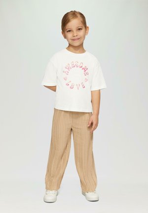 Witte T-shirt met korte mouwen met "Awesome Love" in het roze, gecombineerd met beige geribbelde wijde broek. De outfit wordt aangevuld met witte sneakers.
