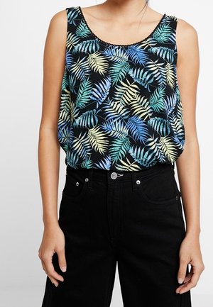 Czarny top bez rękawów z nadrukiem niebieskich, zielonych i żółtych tropikalnych liści, noszony z wysokim stanem czarnych spodni na stojącej osobie.