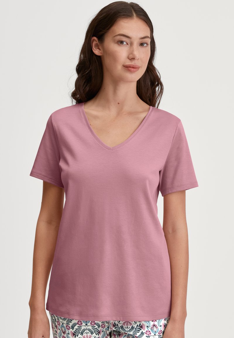 Roze T-shirt met korte mouwen en V-hals, gemaakt van zachte stof. Heeft een comfortabele pasvorm en een gladde textuur, gecombineerd met gepatternde broek.