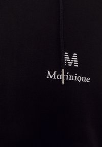 Sweat-shirt à capuche noir avec logo "M" blanc et texte "Matiquique". Tissu doux avec une texture lisse et un accent zippé.
