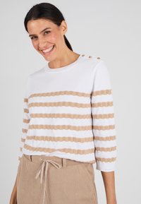 Witte trui met beige horizontale strepen, voorzien van een gestructureerd breipatroon en drie knopen op de schouder. Casual fit.