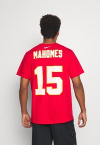 Czerwona koszulka T-shirt z krótkim rękawem wykonana z bawełny, z napisem „MAHOMES” i numerem „15” w żółtej i białej czcionce na plecach. Logo Nike przy dekolcie.