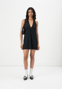 Black halter dress with a keyhole detail, smooth fabric, and A-line shape. Paired with black handbag, white ankle socks, and black shoes.